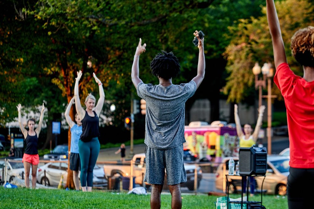 An evening park class with arms raised at dusk.